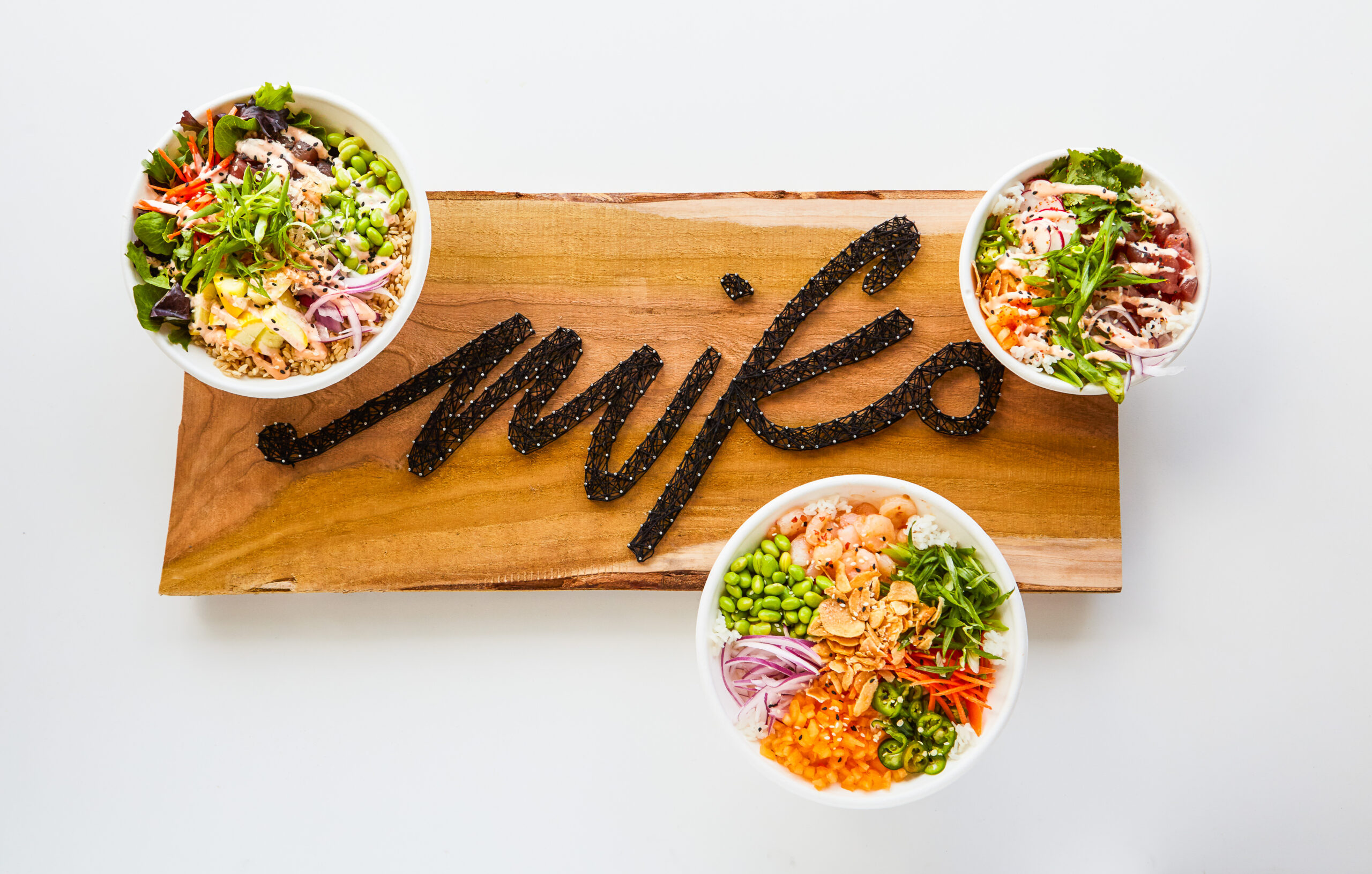 Wood sign featuring string art that spells out "Miko" with 3 bowls that feature vegetable, tuna and spicy chicken sitting around the edges in a graphic visual pattern.
